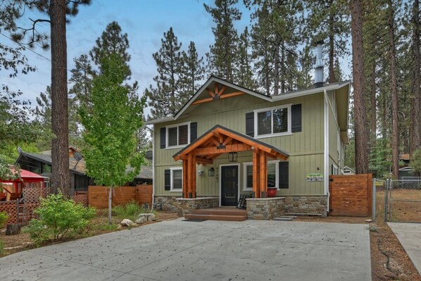 A two-story house with a porch, stone foundation, and a wooden fence.