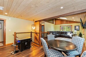 A spacious living area with a wooden ceiling, a black leather sofa, patterned chairs, and a round table.