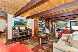 Amplia sala de estar con techo de madera, un televisor de pantalla plana grande, una chimenea y una zona de estar acogedora con sofá y sillones.