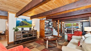 Een ruime woonkamer met een houten plafond, een grote flatscreen-tv, een open haard en een gezellige zithoek met een rode bank en een witte bank.