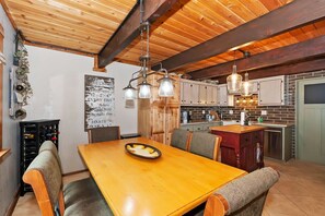A dining area with a wooden table and chairs, a kitchen with brick backsplash, and pendant lighting.