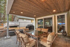 Eine Terrasse im Freien mit einem Glastisch und gepolsterten Stühlen, umgeben von einer Holzw pergola und Blick auf ein Haus.
