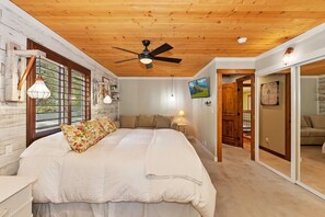 A bedroom with a bed, wooden ceiling, and a view through a window.