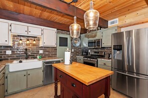 A kitchen with stainless steel appliances, a wooden island, and hanging pendant lights.