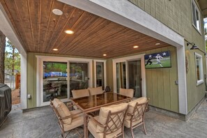 A covered patio with a glass-top table and chairs, a barbecue grill, and a sports-themed wall mural.