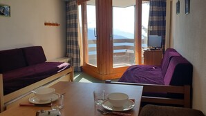 A cozy room with a sofa, a dining table with cups and a teapot, and a television. - Cozy studio near slopes with WIFI (Montvalezan-La Rosière)