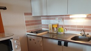 A compact kitchen with a microwave, coffee maker, and kettle on the countertop, a sink, and cabinets with a striped backsplash. - Cozy studio near slopes with WIFI (Montvalezan-La Rosière)