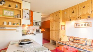 A cozy room with a dining table set for two, a sofa with a colorful cushion, wooden cabinets, and a microwave. - Comfortable apartment near slopes with WIFI (Montvalezan-La Rosière)
