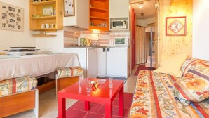 A cozy living room with a sofa, a red table, and a kitchen area with a microwave and cabinets. - Comfortable apartment near slopes with WIFI (Montvalezan-La Rosière)
