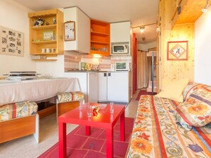 A cozy living room with a sofa, a red table, and a kitchen area with a microwave and cabinets. - Comfortable apartment near slopes with WIFI (Montvalezan-La Rosière)