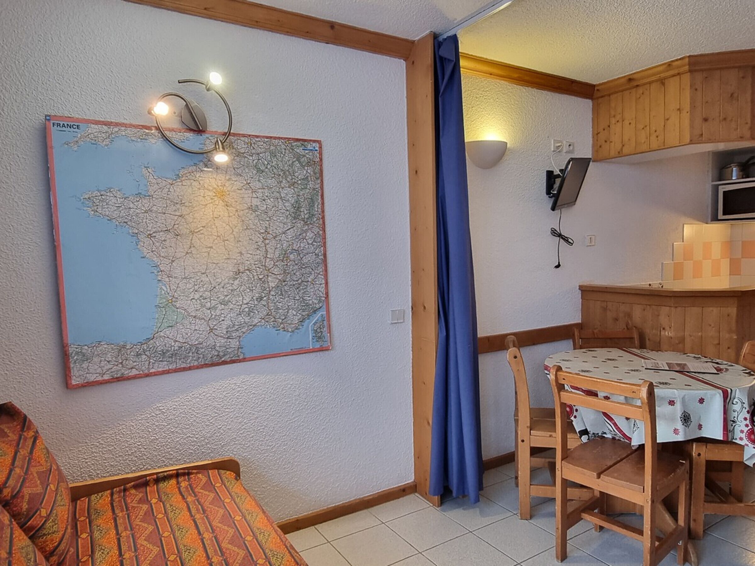 Um quarto acolhedor com um mapa grande na parede, uma mesa de jantar de madeira com cadeiras e uma cortina azul.