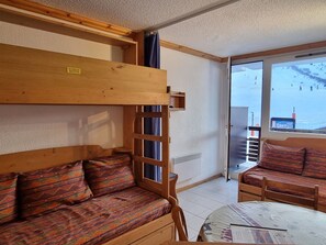 A cozy room with a bunk bed, a sofa, a table, and a view of a snowy landscape through a large window.
