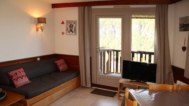 A cozy room with a sofa, a TV, a dining table, and a balcony with a wooden railing.