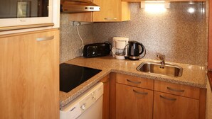 A compact kitchen with wooden cabinets, a built-in oven, a coffee maker, and a sink.