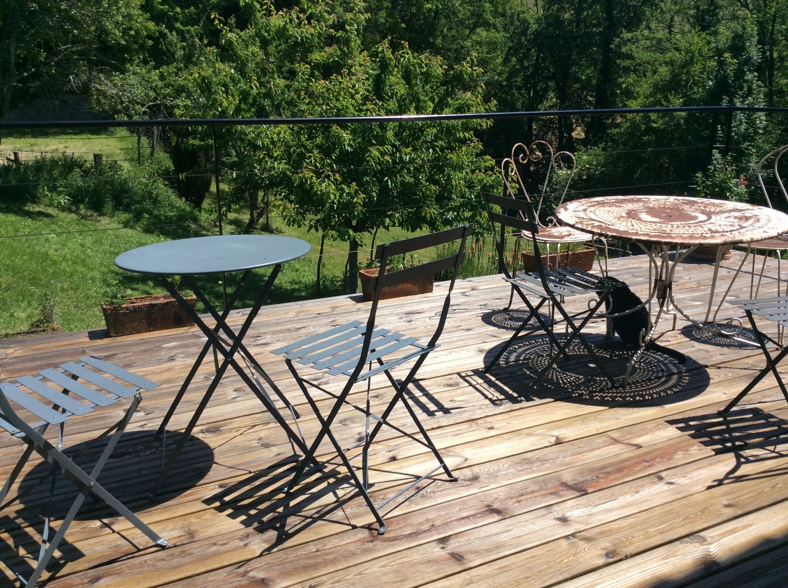 Une terrasse extérieure avec une table ronde et des chaises, entourée d’une plateforme en bois et offrant une vue sur un paysage verdoyant.