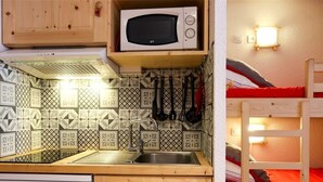Una cucina compatta con forno a microonde, lavello e lavastoviglie. Si intravede un letto a castello nella stanza adiacente.