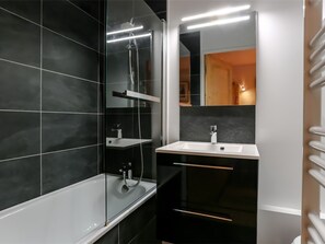 Une salle de bain moderne avec une douche à parois de verre, un lavabo blanc et un mur recouvert de carreaux foncés.