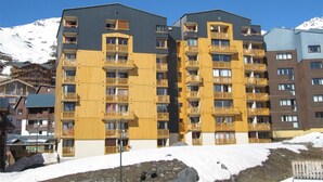 Un hotel a più piani con balconi, una pista da sci sullo sfondo e un cielo blu limpido.
