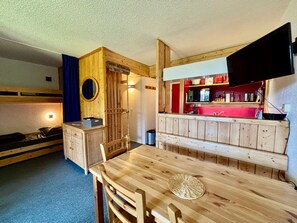 A compact room with a wooden bunk bed, a small kitchenette with a TV, and a dining area with a table and chairs. - Apartment near slopes with balcony and wifi (Les Arcs 1800)