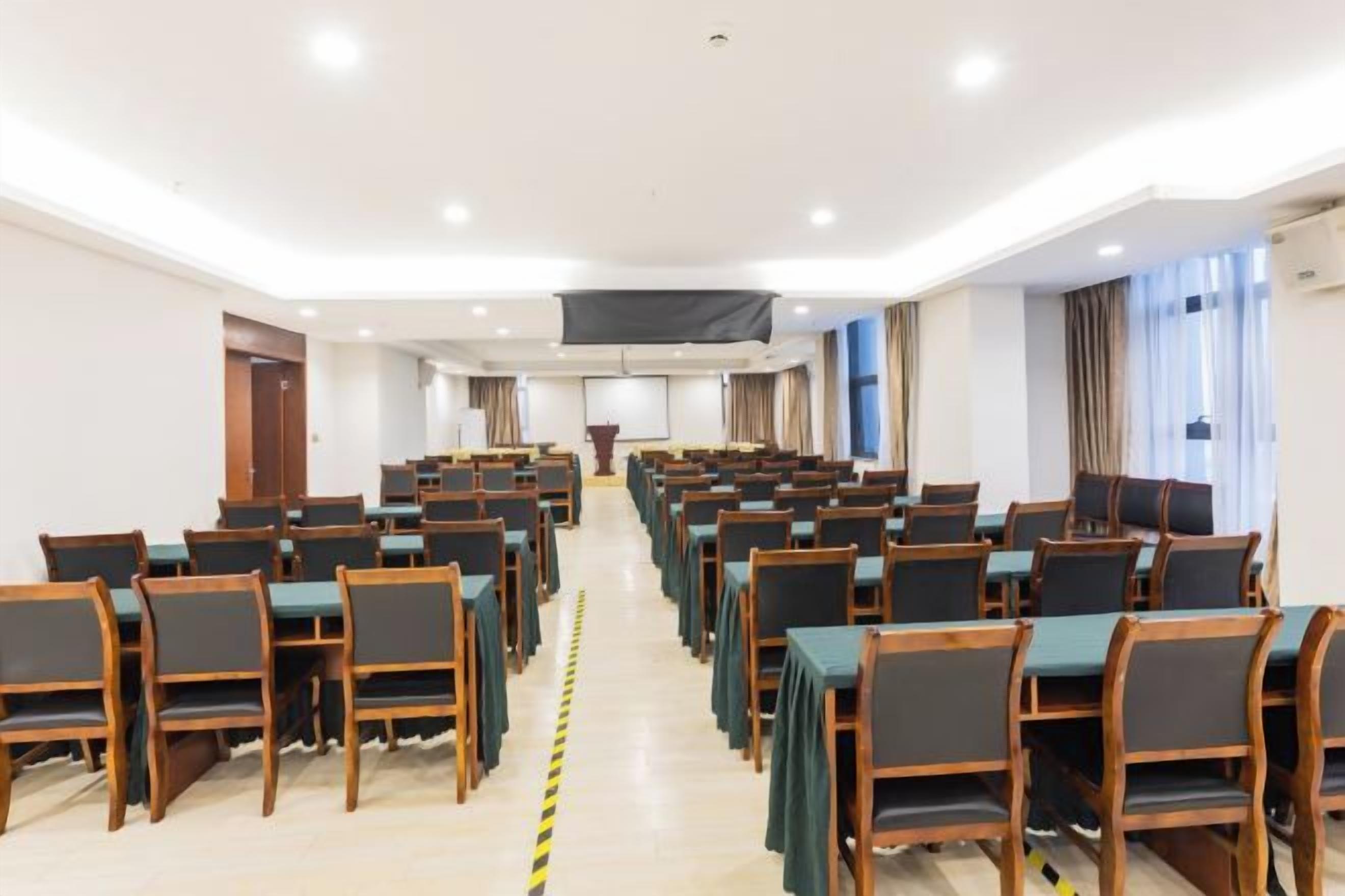 A conference room with rows of tables and chairs, a podium, and a large screen at the front.