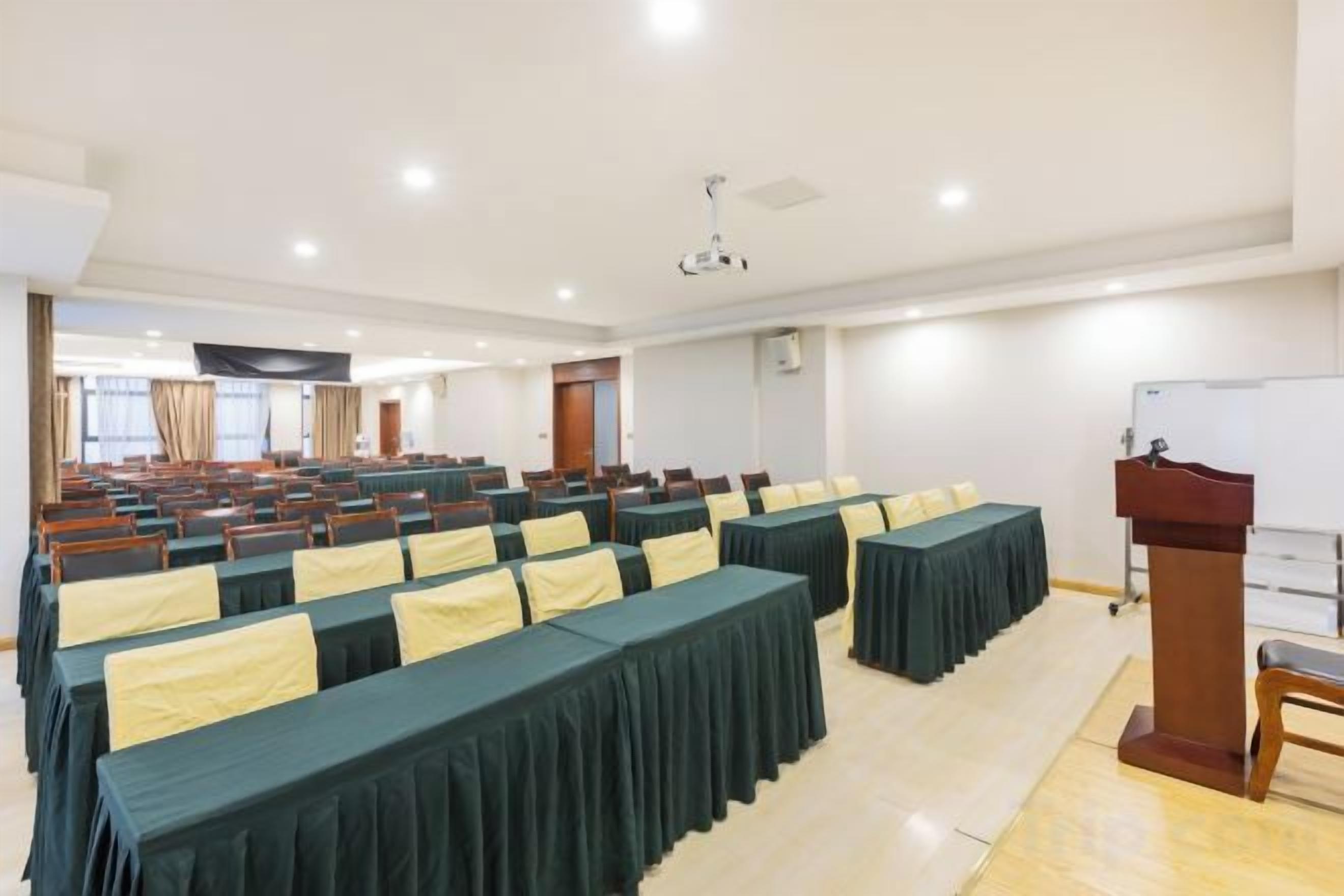 Uma sala de conferências com fileiras de mesas, um pódio e um quadro branco.
