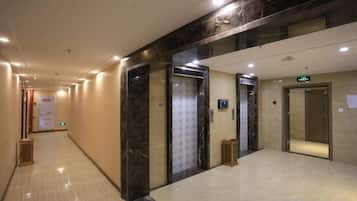 Corredor de hotel com piso de mármore, elevadores e uma placa indicando o caminho para a recepção.
