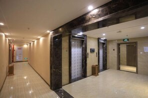 Een hotelgangen met marmeren vloer, liften en een bordje dat de richting naar de lobby aangeeft.