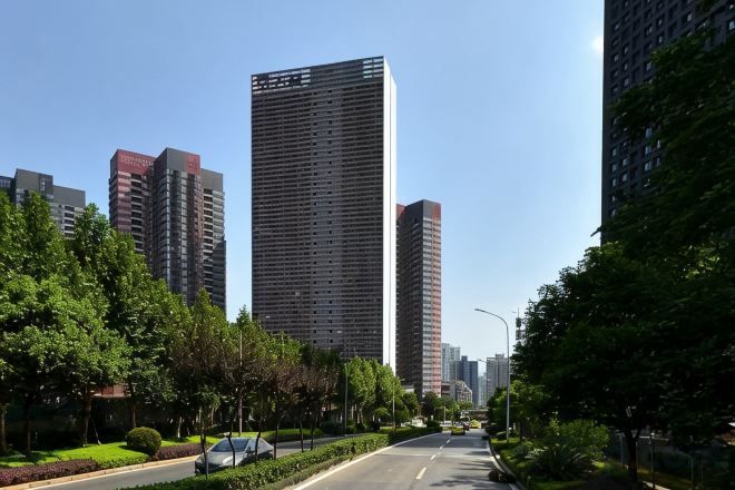 A city street lined with tall buildings, trees, and a clear sky.