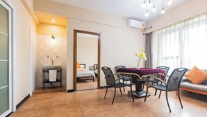 Una habitación de hotel moderna con zona de comedor, una pequeña cocina y un gran ventanal con cortinas.