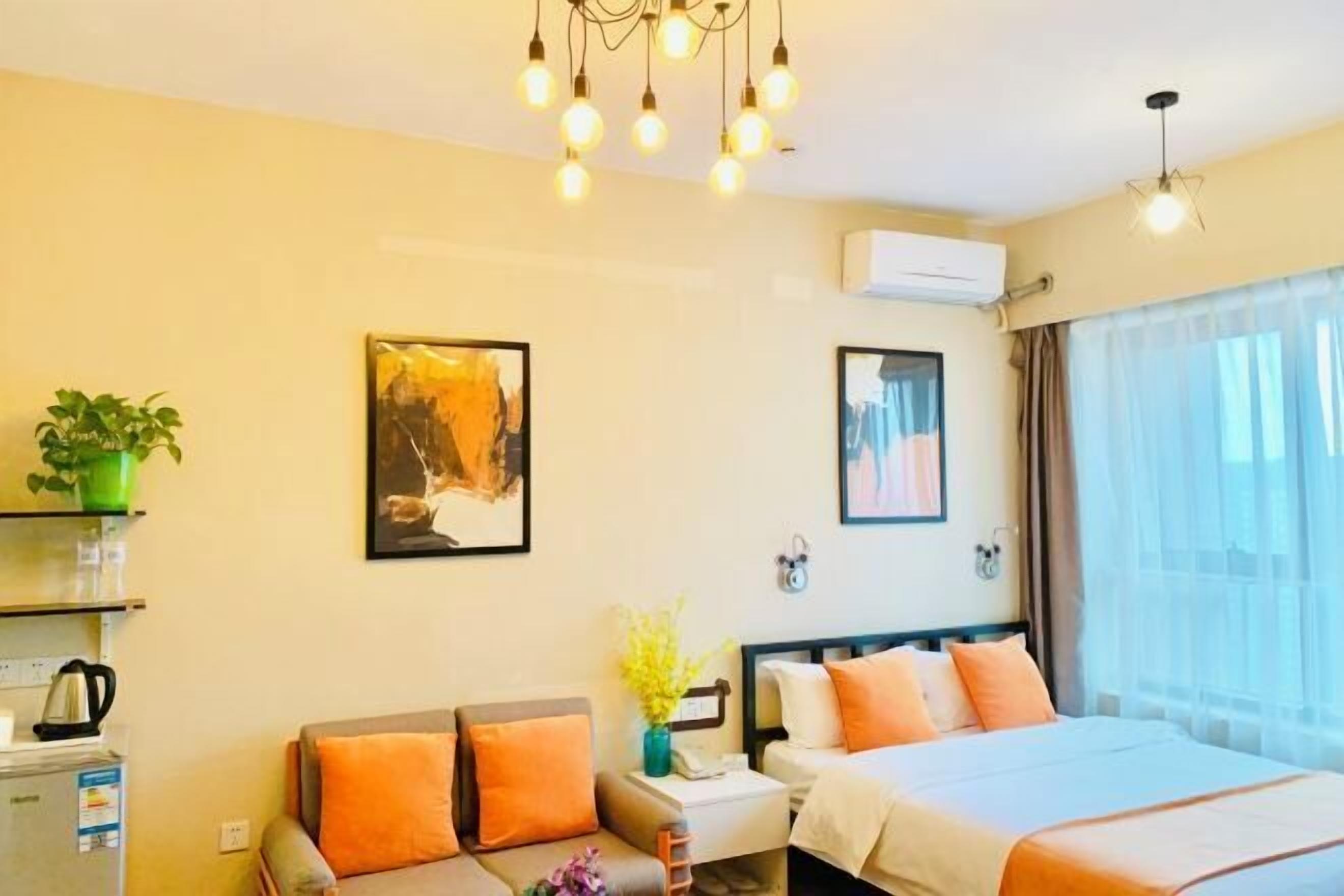 A hotel room with a bed, a sofa, a small table with a plant, and artwork on the walls.