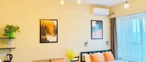 A hotel room with a bed, a sofa, a small table with a plant, and artwork on the walls.