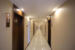 A hotel hallway with doors on both sides, numbered signs, and a lighted ceiling.