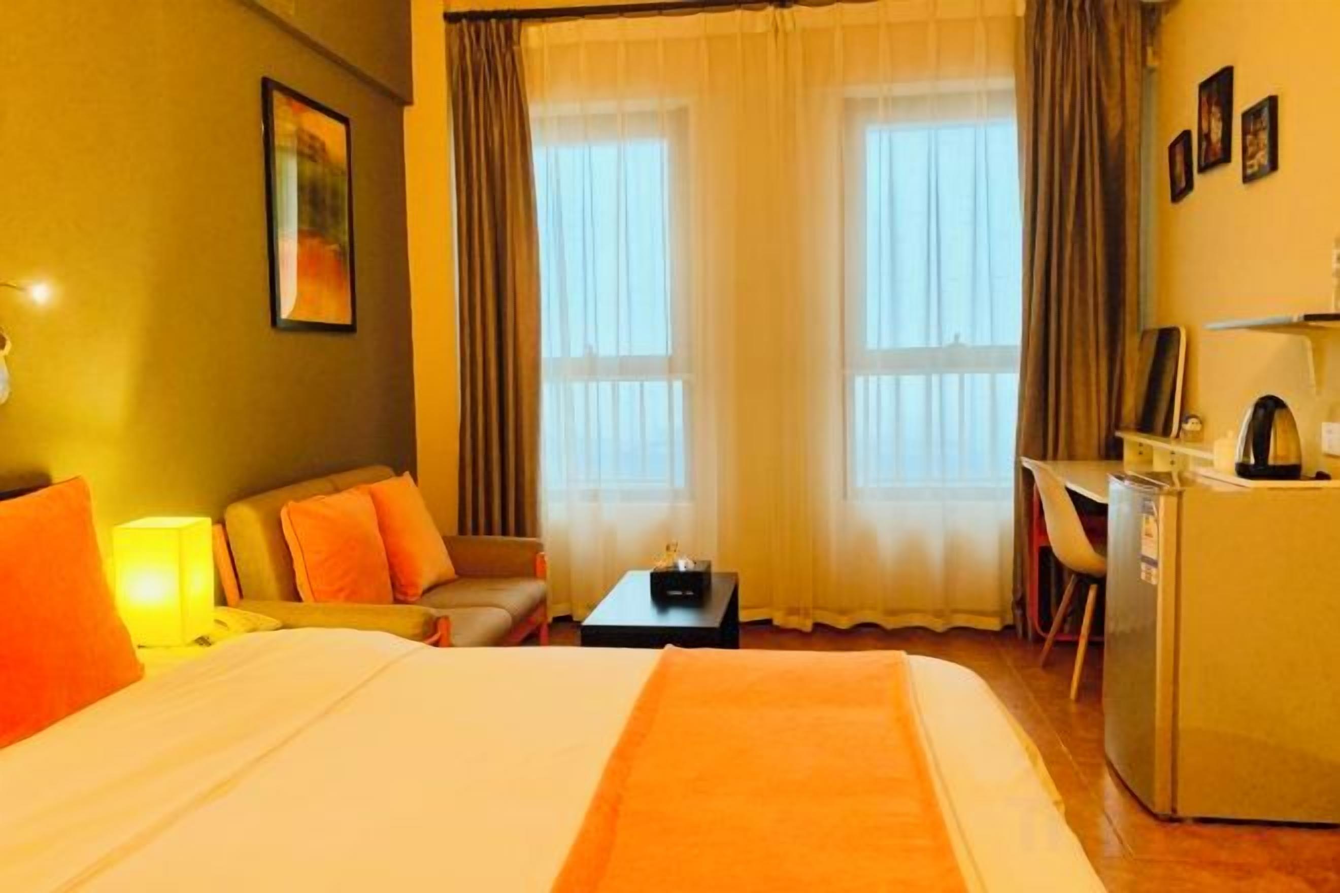 A hotel room with a bed, a desk, a chair, a small table, and a refrigerator.