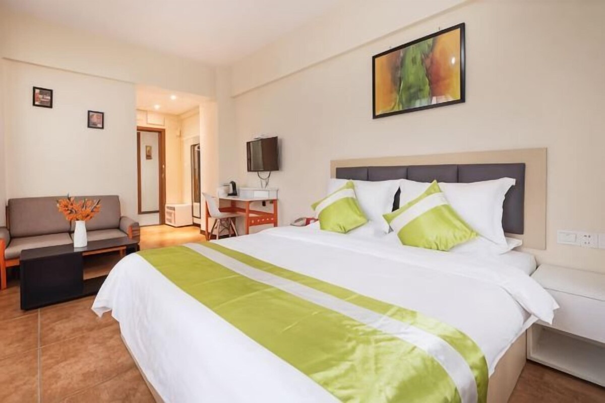 Et hotelværelse med seng, skrivebord, stol og fjernsyn.