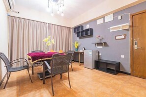 A dining area with a table, chairs, a refrigerator, and a wall-mounted shelf unit.