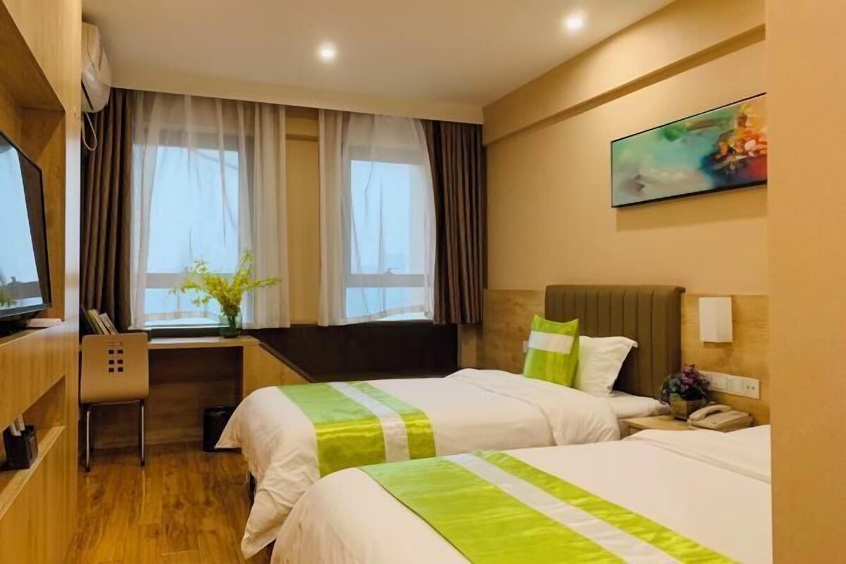 A hotel room with two beds, a desk, a chair, a TV, and a window with curtains.