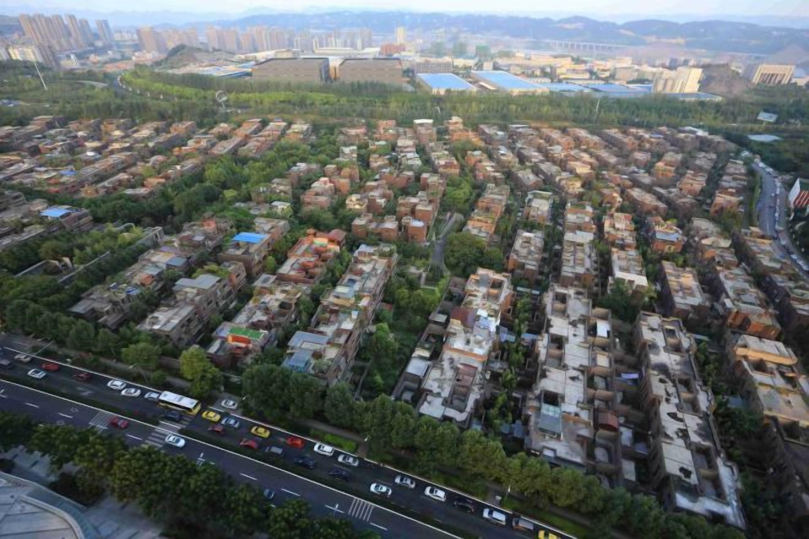 An aerial view of a residential area with organized housing blocks, a main road, and distant buildings.
