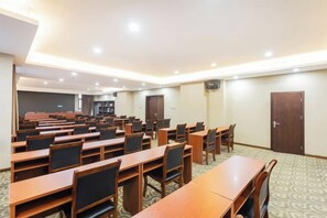 Un salón de conferencias con varias mesas y sillas, piso alfombrado y una puerta al fondo.