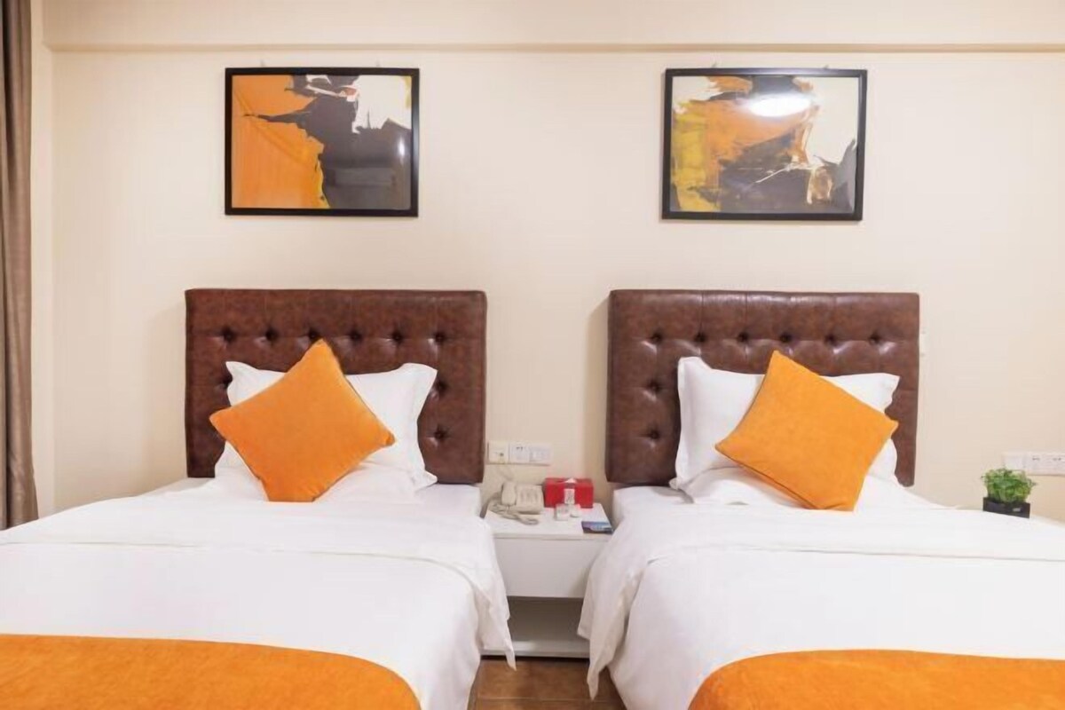 Een hotelkamer met twee bedden, elk met een bruin hoofdeinde en witte beddengoed. Boven de bedden hangen twee ingelijste foto’s.