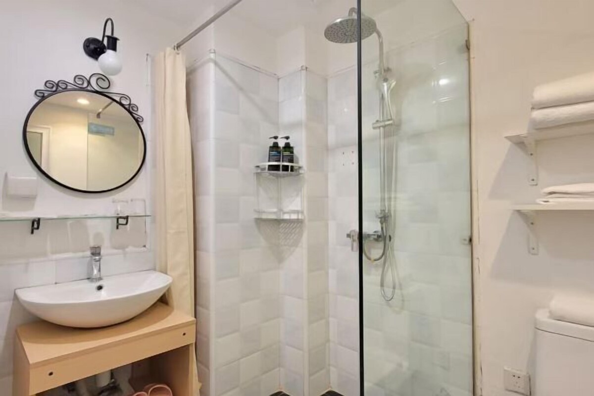 Een moderne badkamer met een glazen douchecabine, een ronde spiegel en een wit wastafelmeubel.