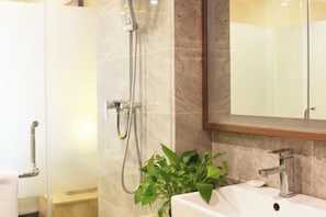 A bathroom with a glass shower enclosure, a sink with a modern faucet, and a potted plant.