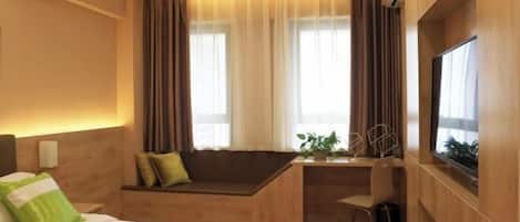 A hotel room with a bed, a desk, a chair, a TV, and a window with curtains.