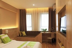 A hotel room with a bed, a desk, a chair, a TV, and a window with curtains.