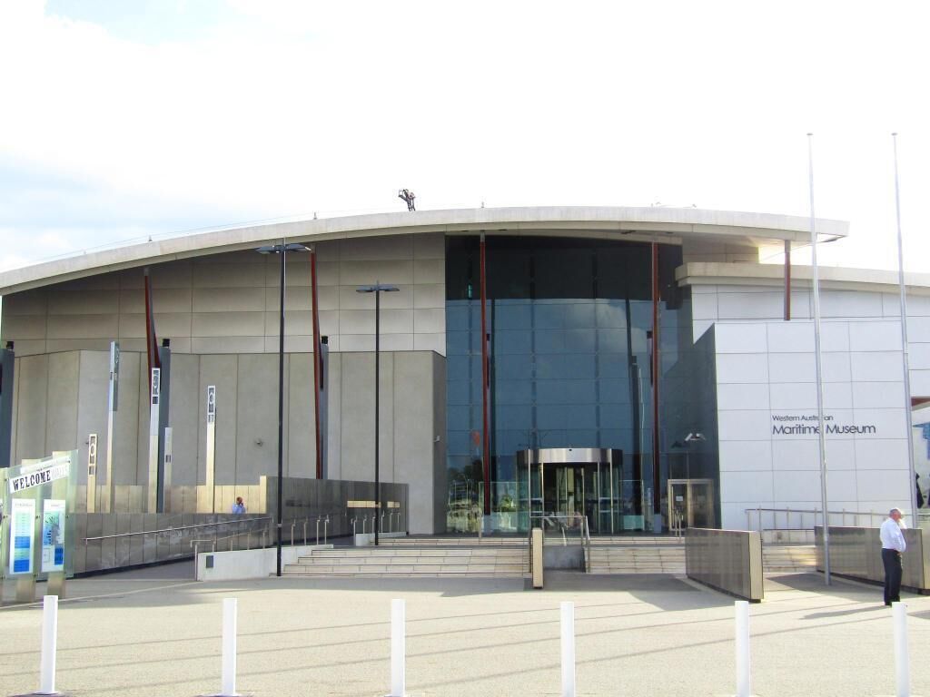Een modern gebouw met een gebogen gevel, een glazen entree en een bord waarop staat: "Western Australian Maritime Museum".