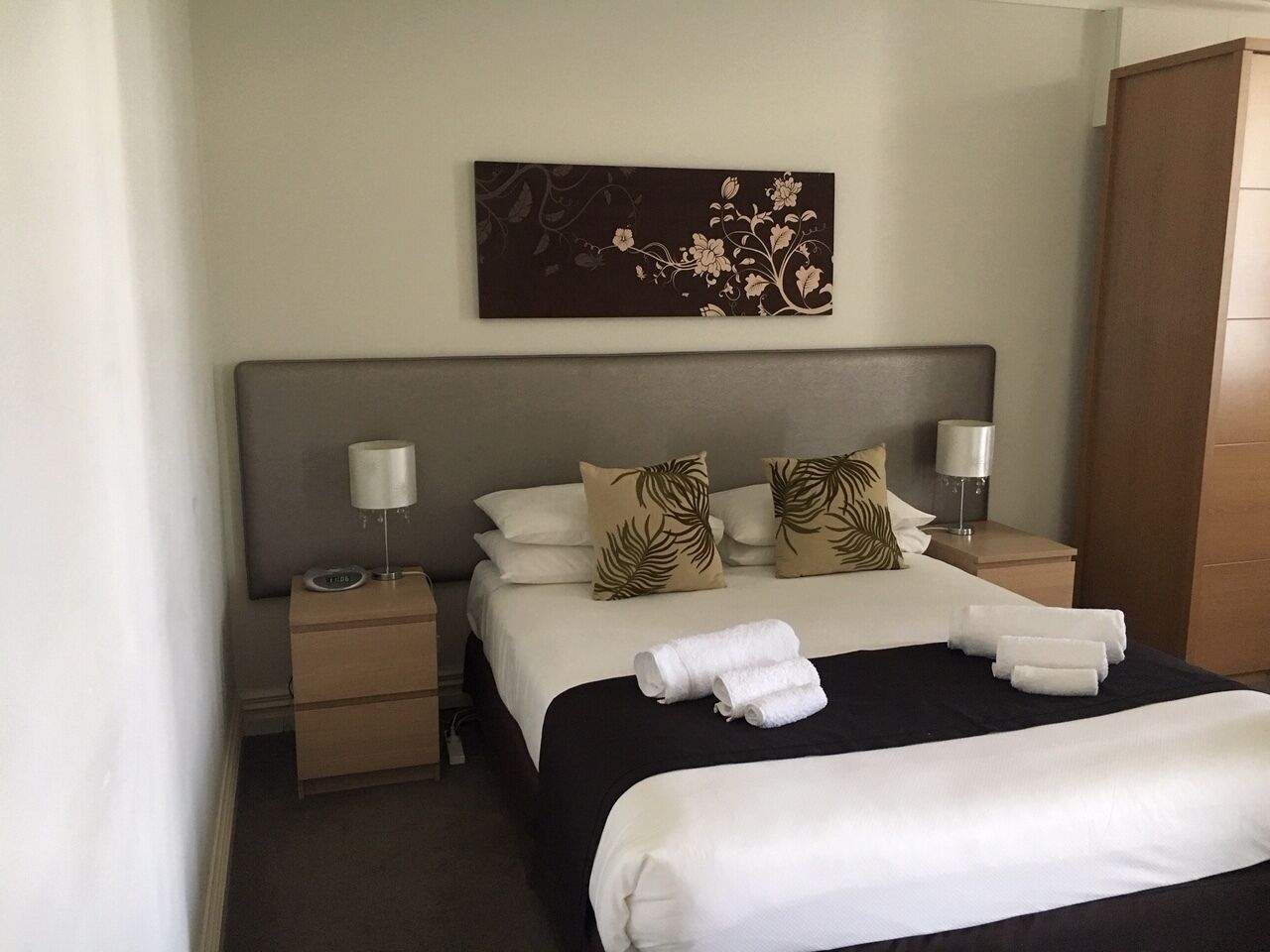 A hotel room with a bed, two nightstands, a lamp, and a painting on the wall.