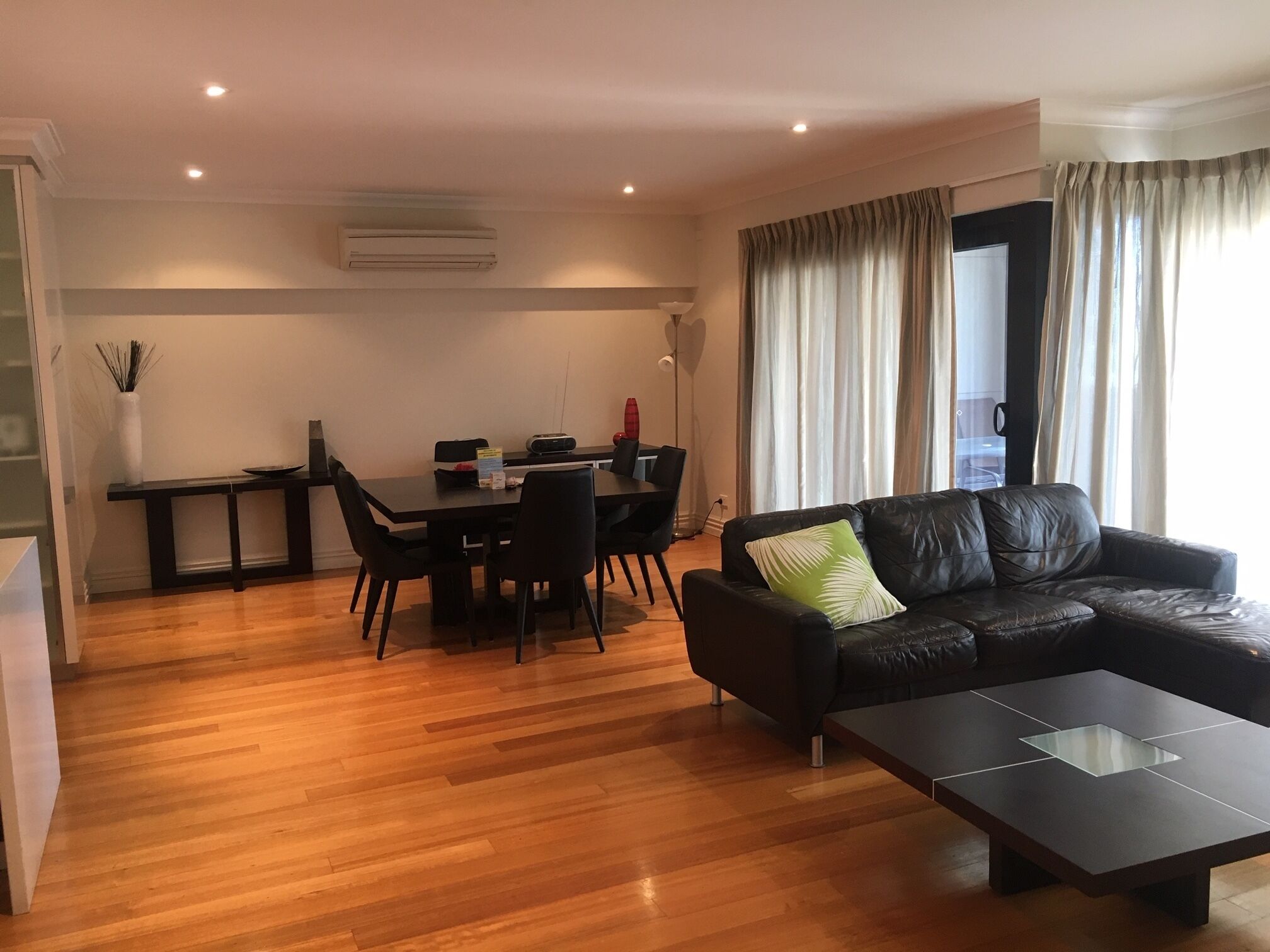 A modern living room with a black leather sofa, a glass-top coffee table, and a dining area with a black table and chairs.