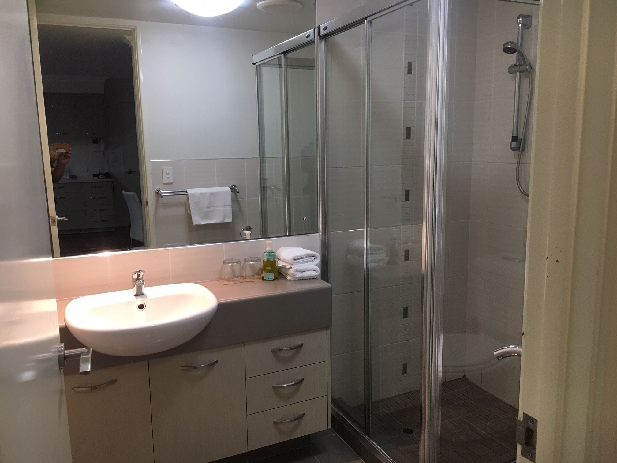 Une salle de bain moderne avec un lavabo blanc, un miroir, une douche en verre et un porte-serviettes.
