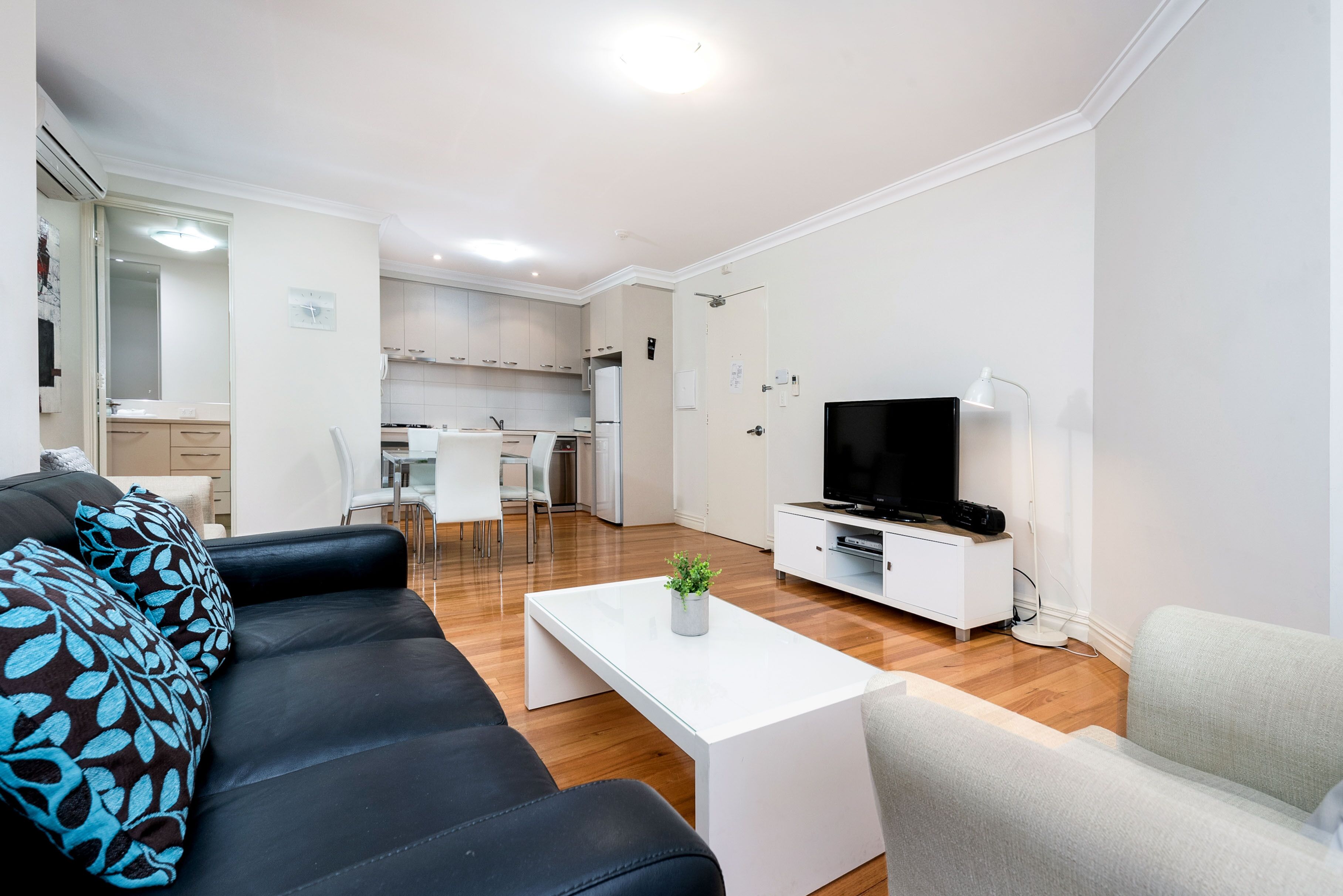 A modern living room with a black leather sofa, a white coffee table with a plant, a TV, and a white cabinet.
