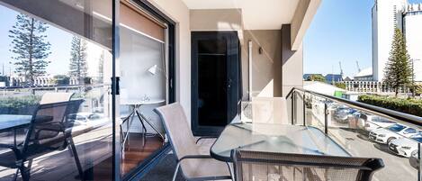 A balcony with a glass table and chairs, a sliding door, and a view of a cityscape including a tall building.