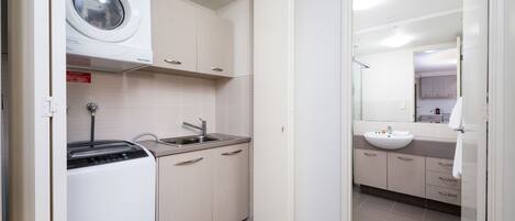 A compact kitchen with a washing machine, sink, and cabinets.